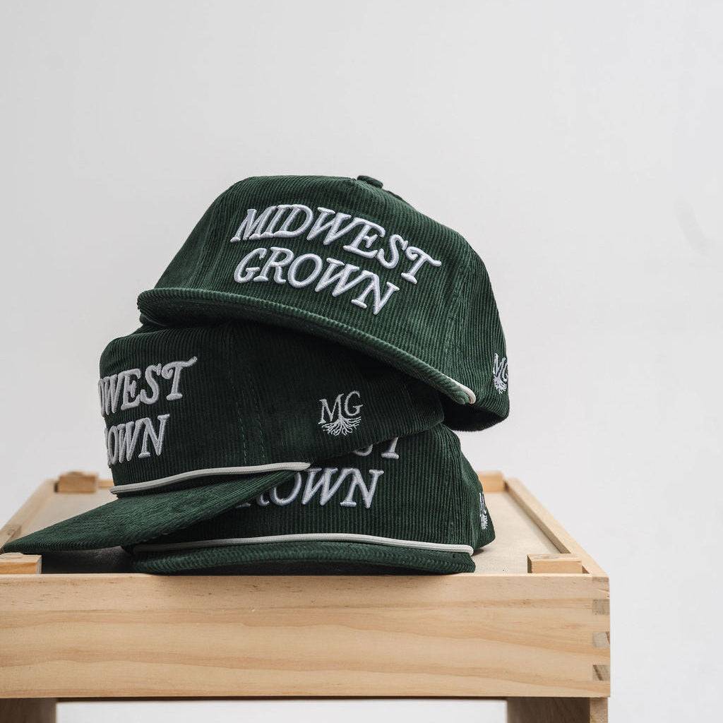 Green hats with 'Midwest Grown' text on a wooden surface