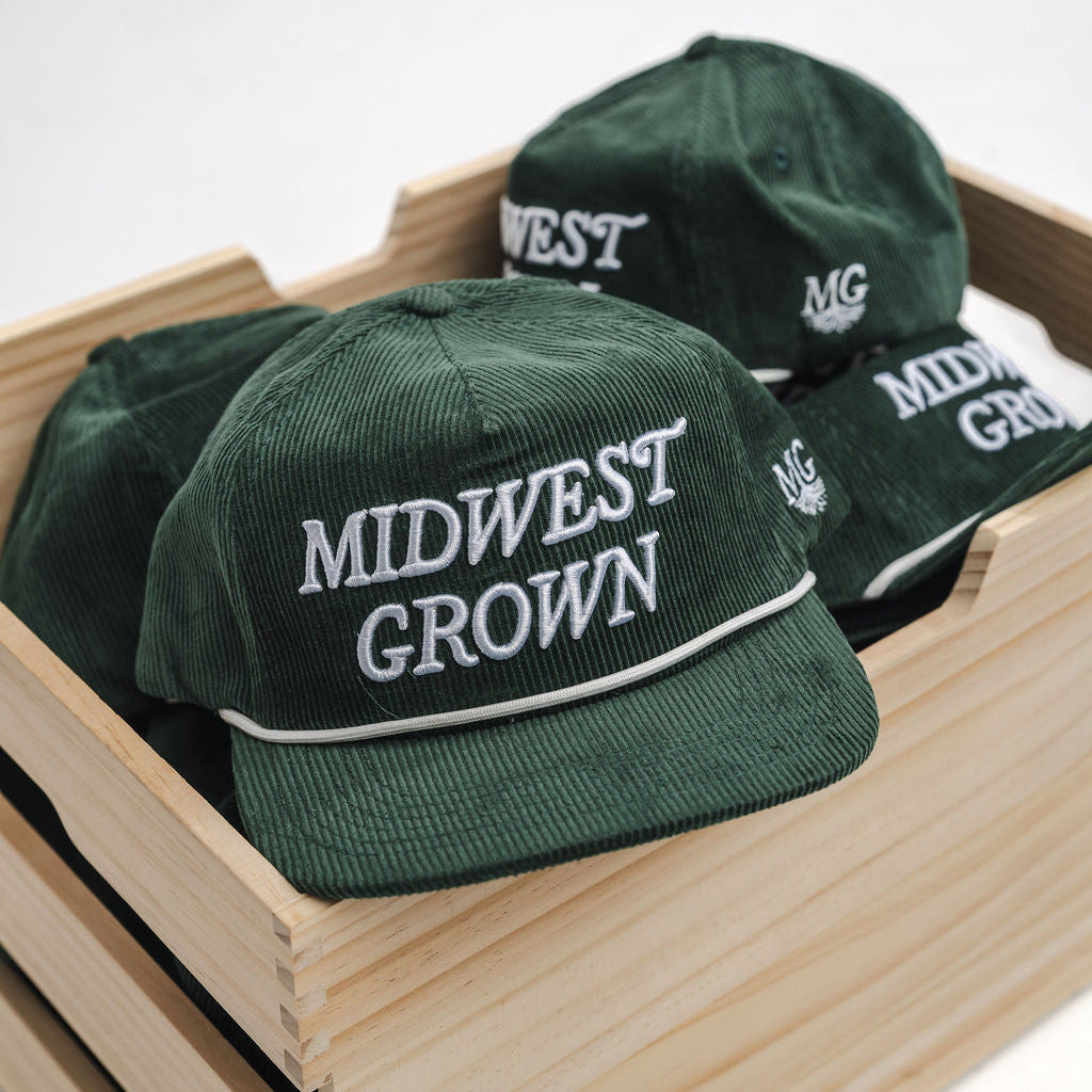 Green caps with 'Midwest Grown' text in a wooden crate on a white background