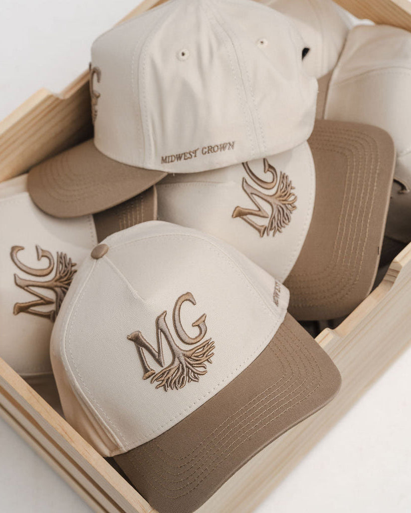 Set of beige and brown caps with 'Midwest Grown' logo in a wooden box on a light background