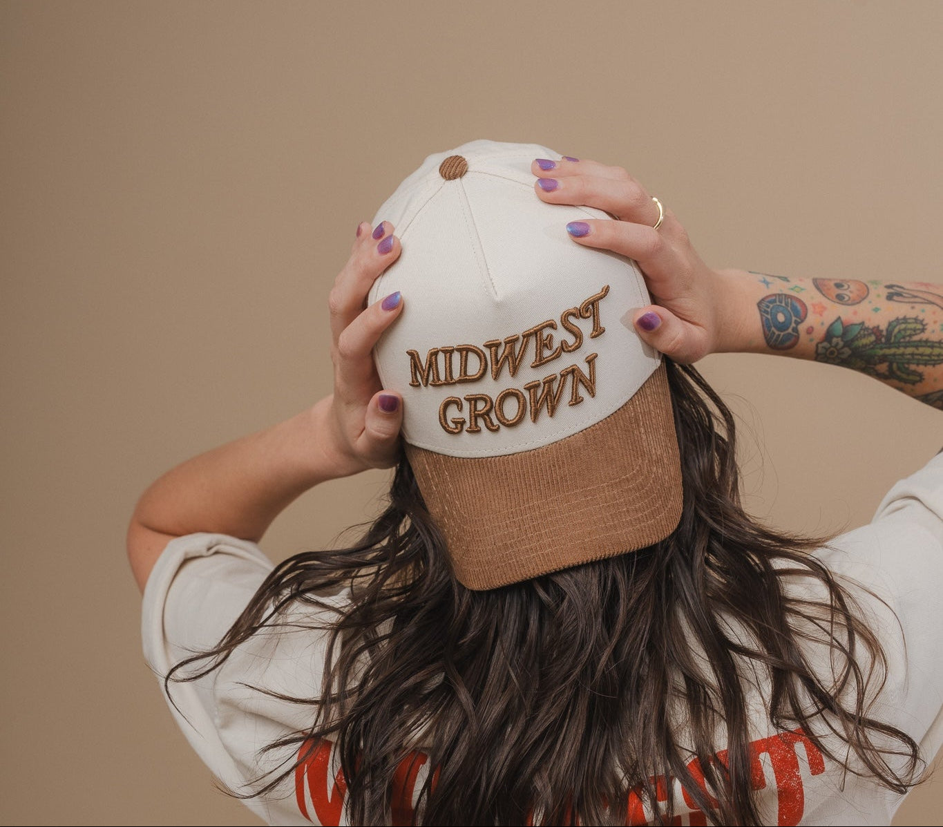 Person holding a cap with 'Midwest Grown' text against a beige background