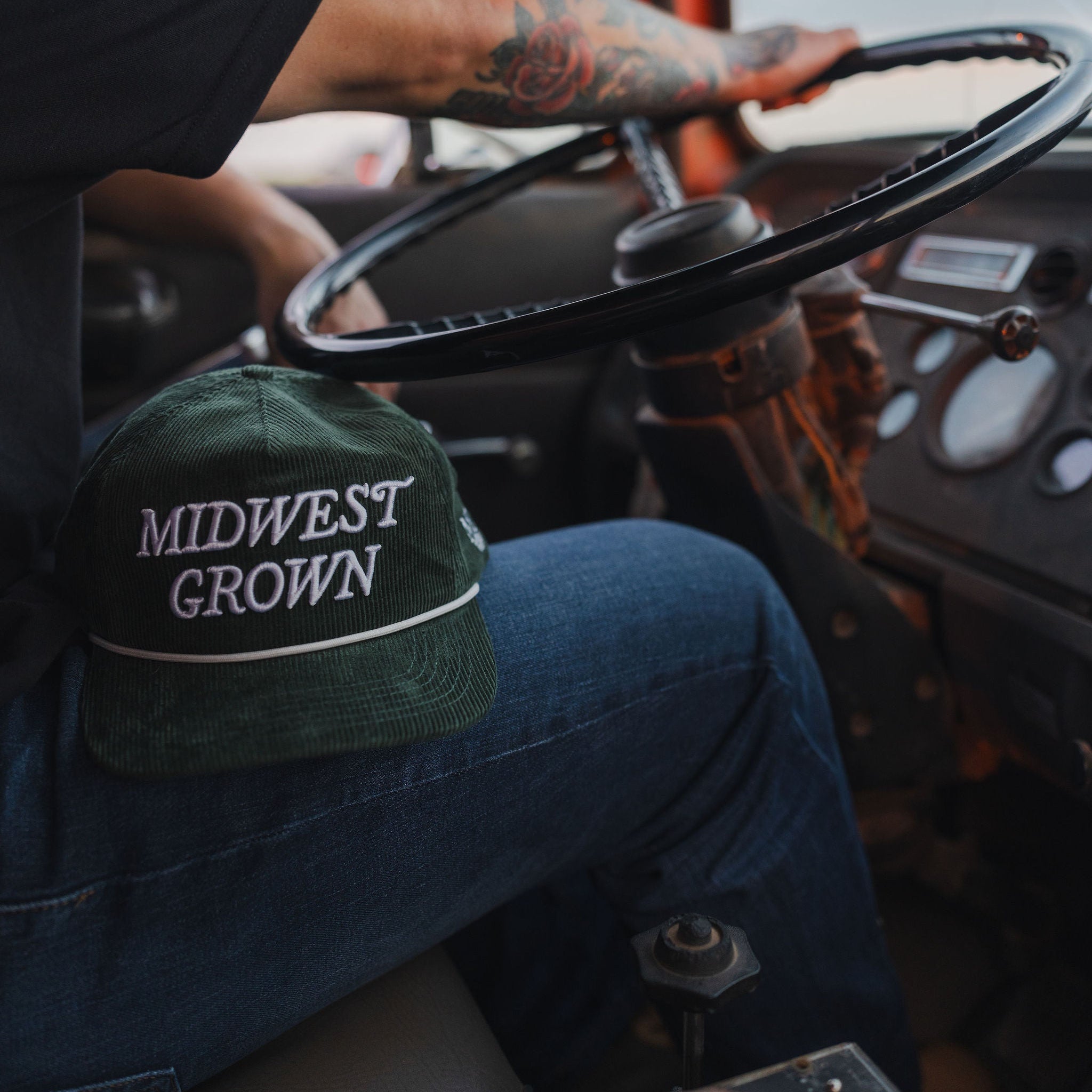 Person sitting inside a vehicle with a 'Midwest Grown' cap on their lap.