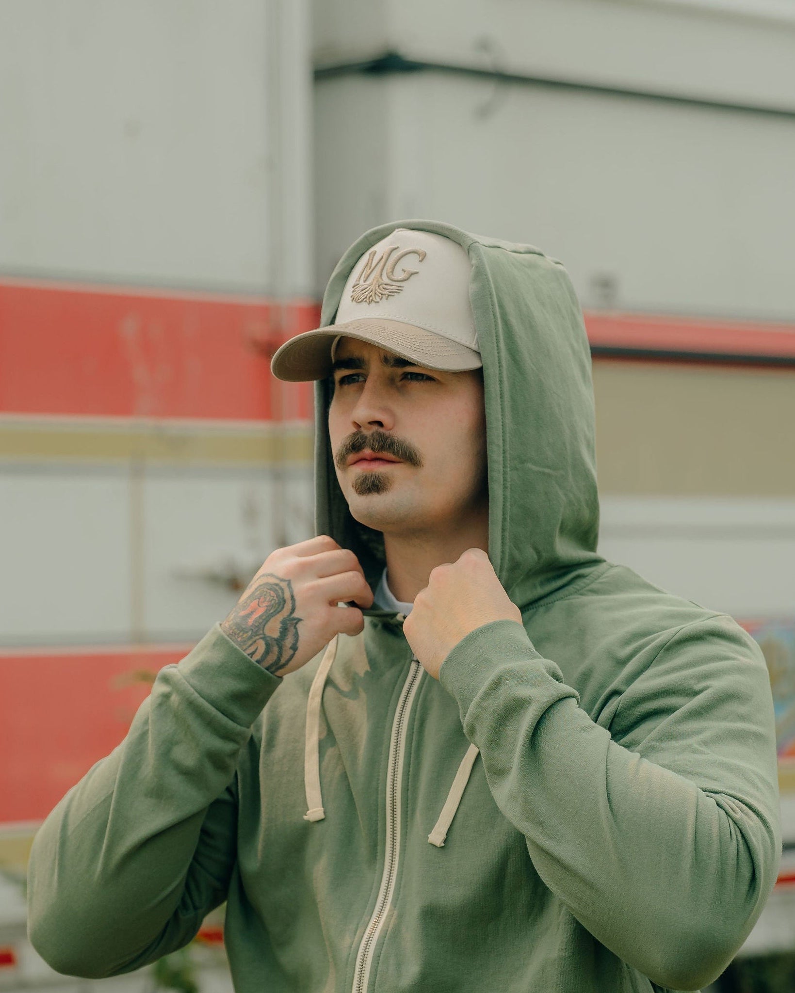 Man wearing a green hoodie and beige Midwest Grown cap in front of a colorful truck.