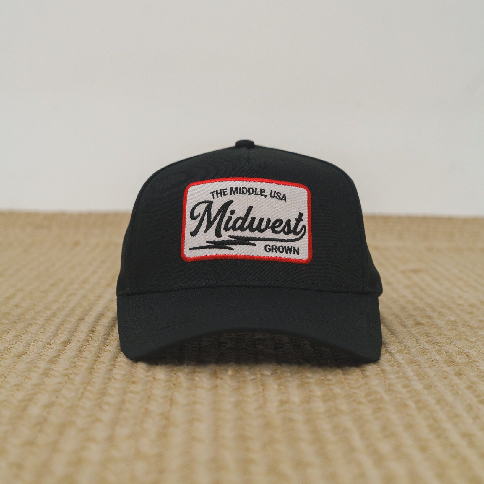 Black cap with 'Midwest Grown' patch on a wooden surface