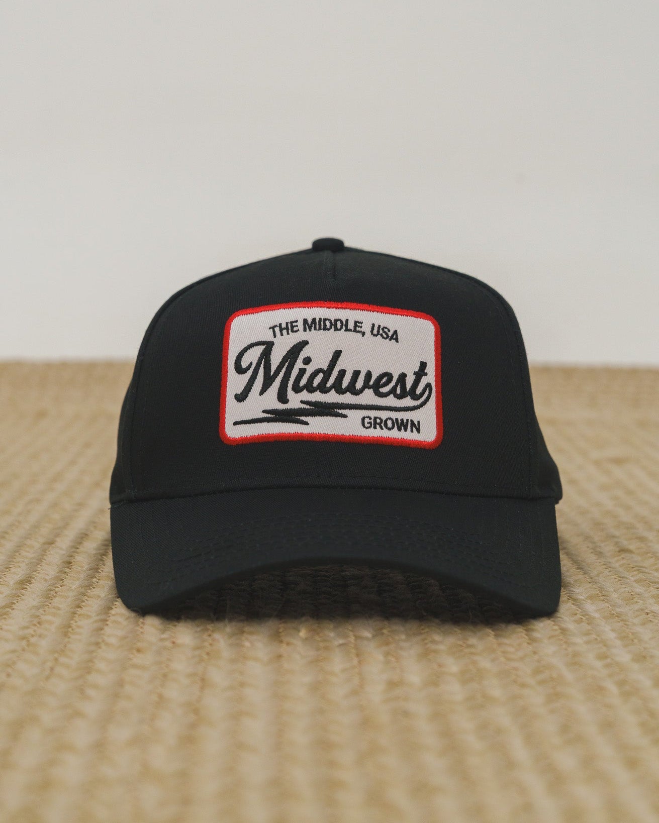 Black cap with 'Midwest Grown' patch on a wooden surface