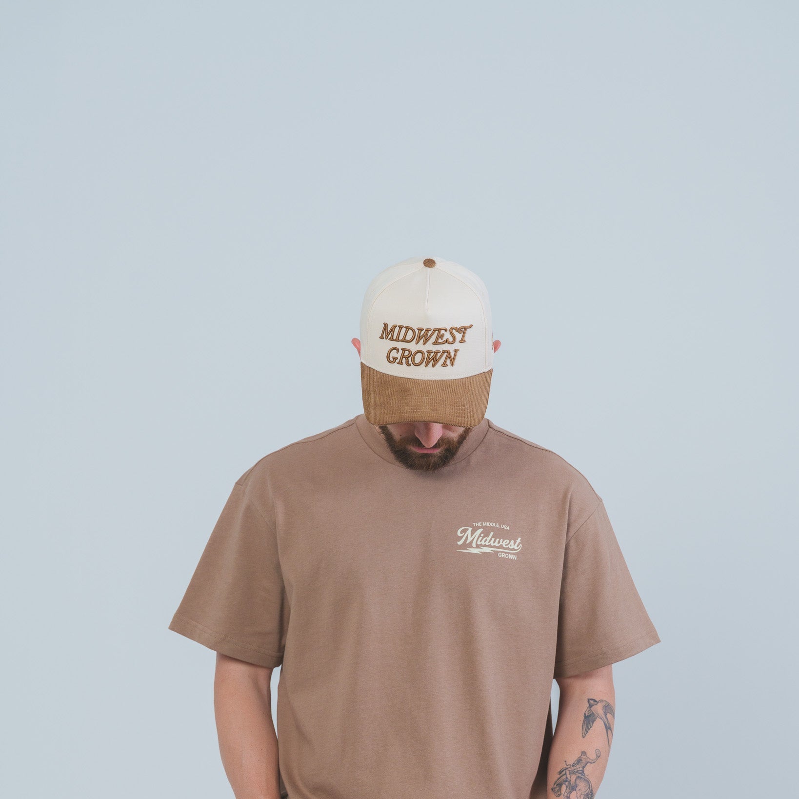 Person wearing a brown t-shirt and cap with 'Midwest Grown' text on a light blue background