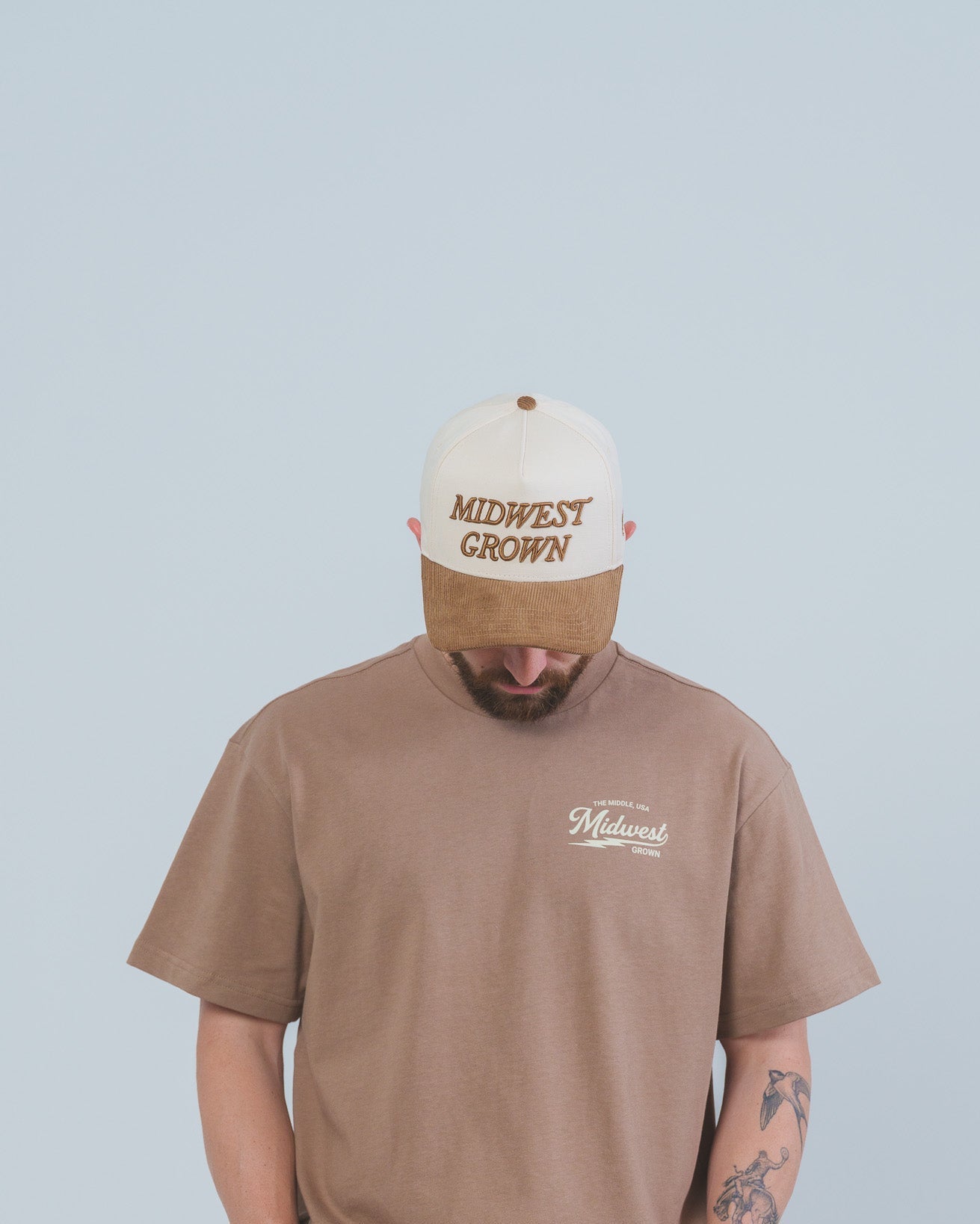 Person wearing a brown t-shirt and cap with 'Midwest Grown' text on a light blue background