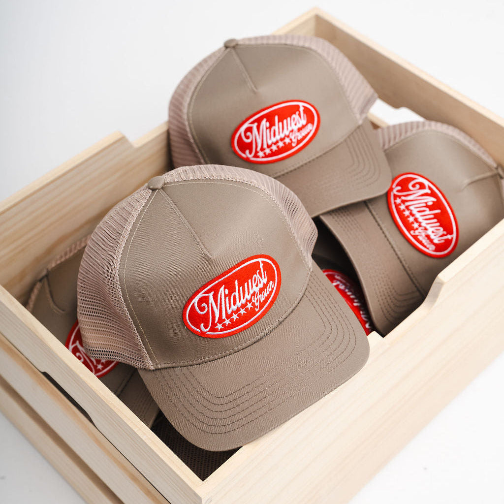 Three beige Midwest Grown caps with red logos in a wooden box on a light gray background