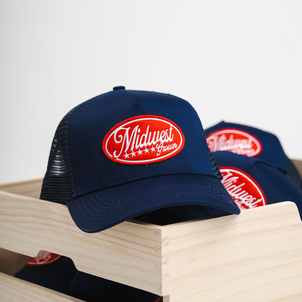 Two navy blue Midwest Grown hats with a red logo on a wooden surface