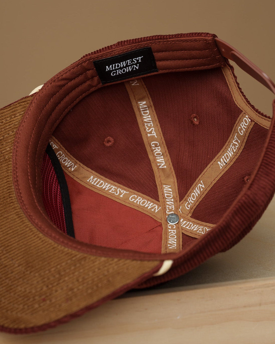 Maroon Midwest Grown baseball cap with visible branding on a wooden surface and beige background