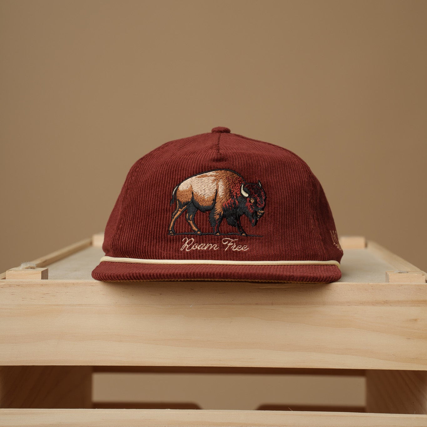 Maroon Midwest Grown cap with a bison design on a wooden surface against a beige background