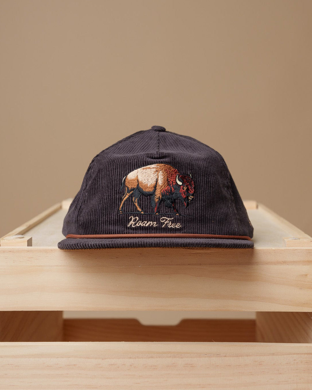 Midwest Grown Cap with a bison design on a wooden crate against a beige background
