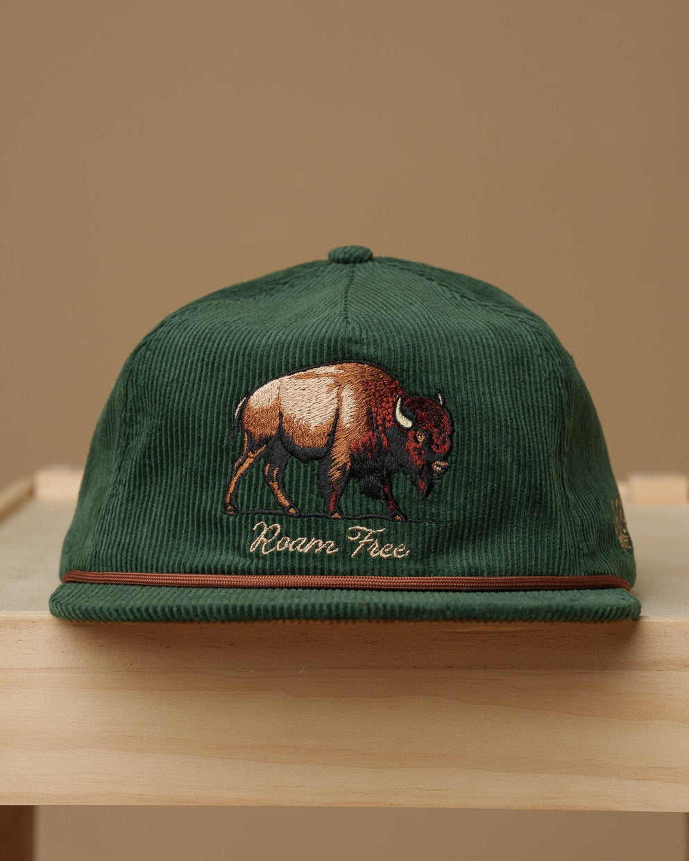 Midwest Grown Green cap with a bison design on a wooden crate against a beige background