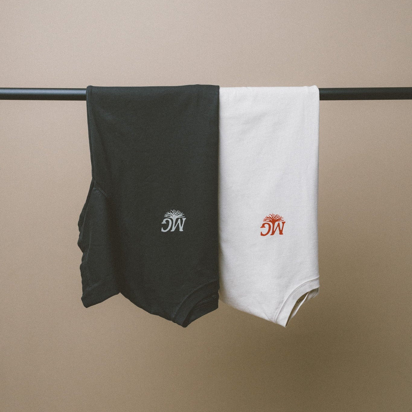 Black and white tees with Midwest Grown logos hanging on a rod against a beige background