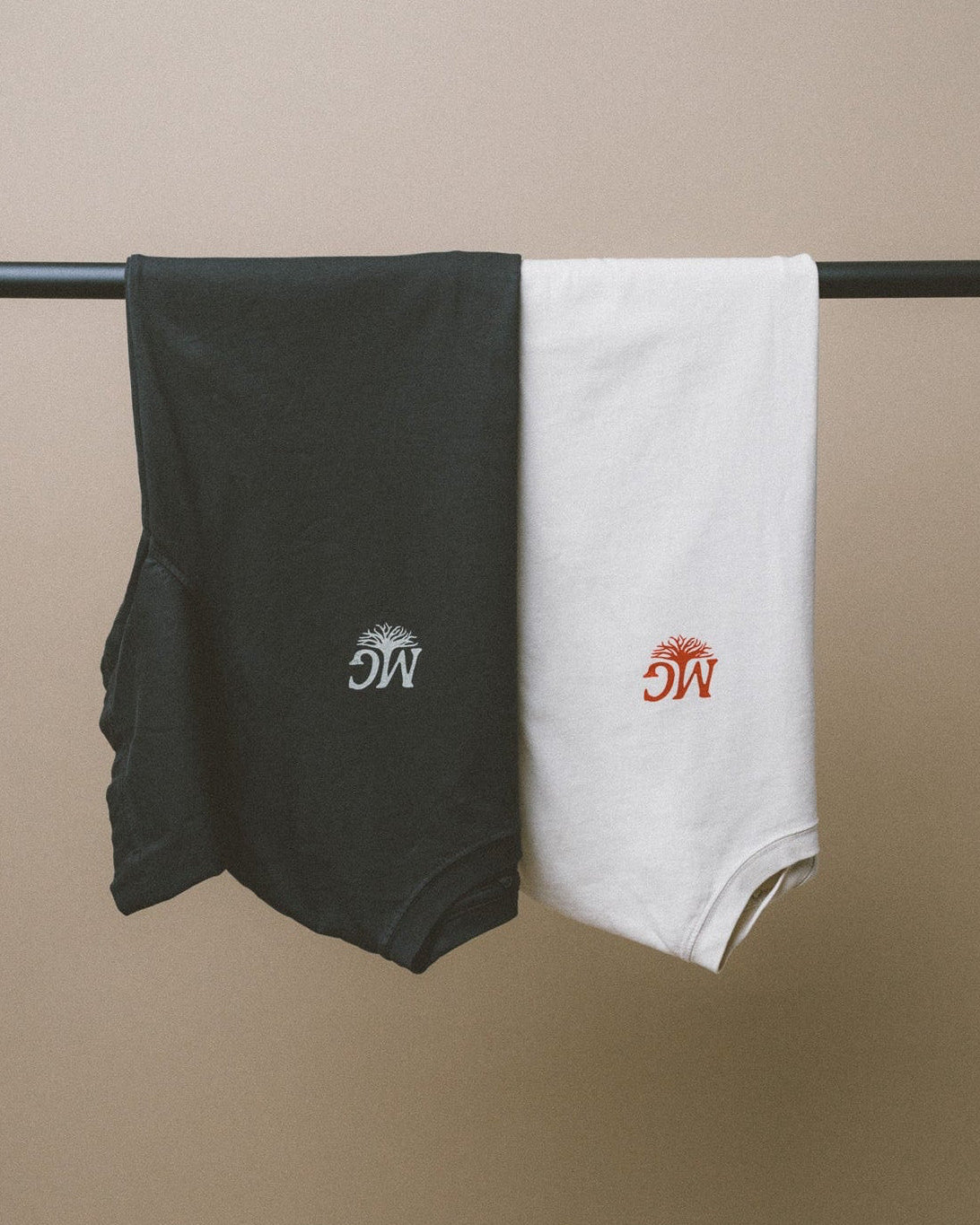 Black and white tees with Midwest Grown logos hanging on a rod against a beige background