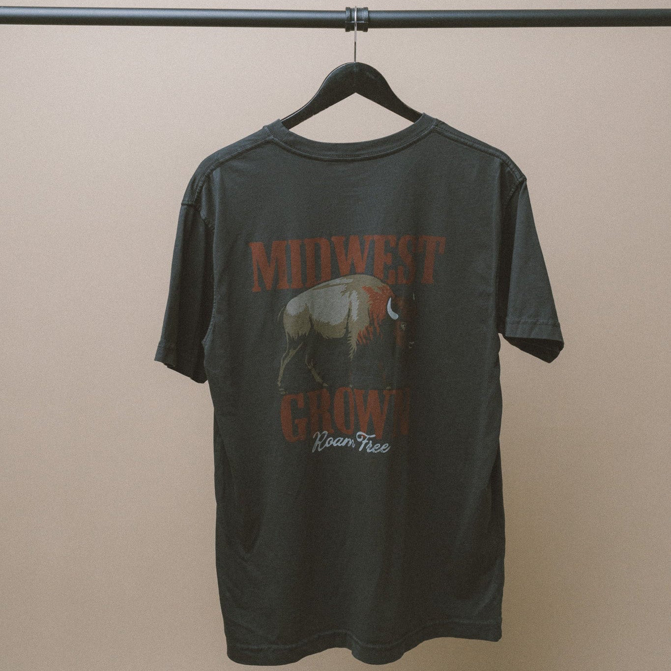 Black Midwest Grown t-shirt with Bison graphic design and text on a hanger against a beige wall
