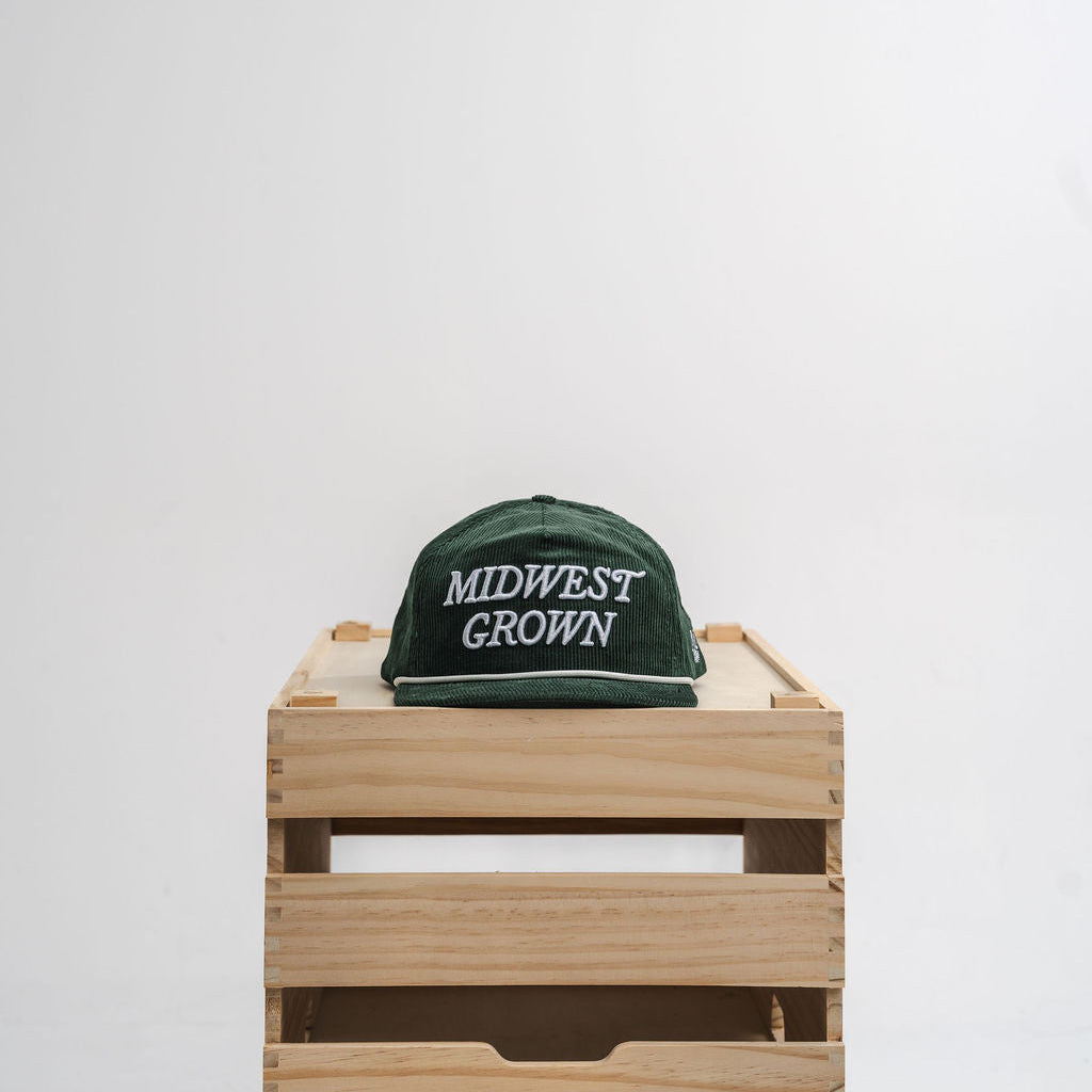 Green hat with 'Midwest Grown' text on a wooden crate against a white background