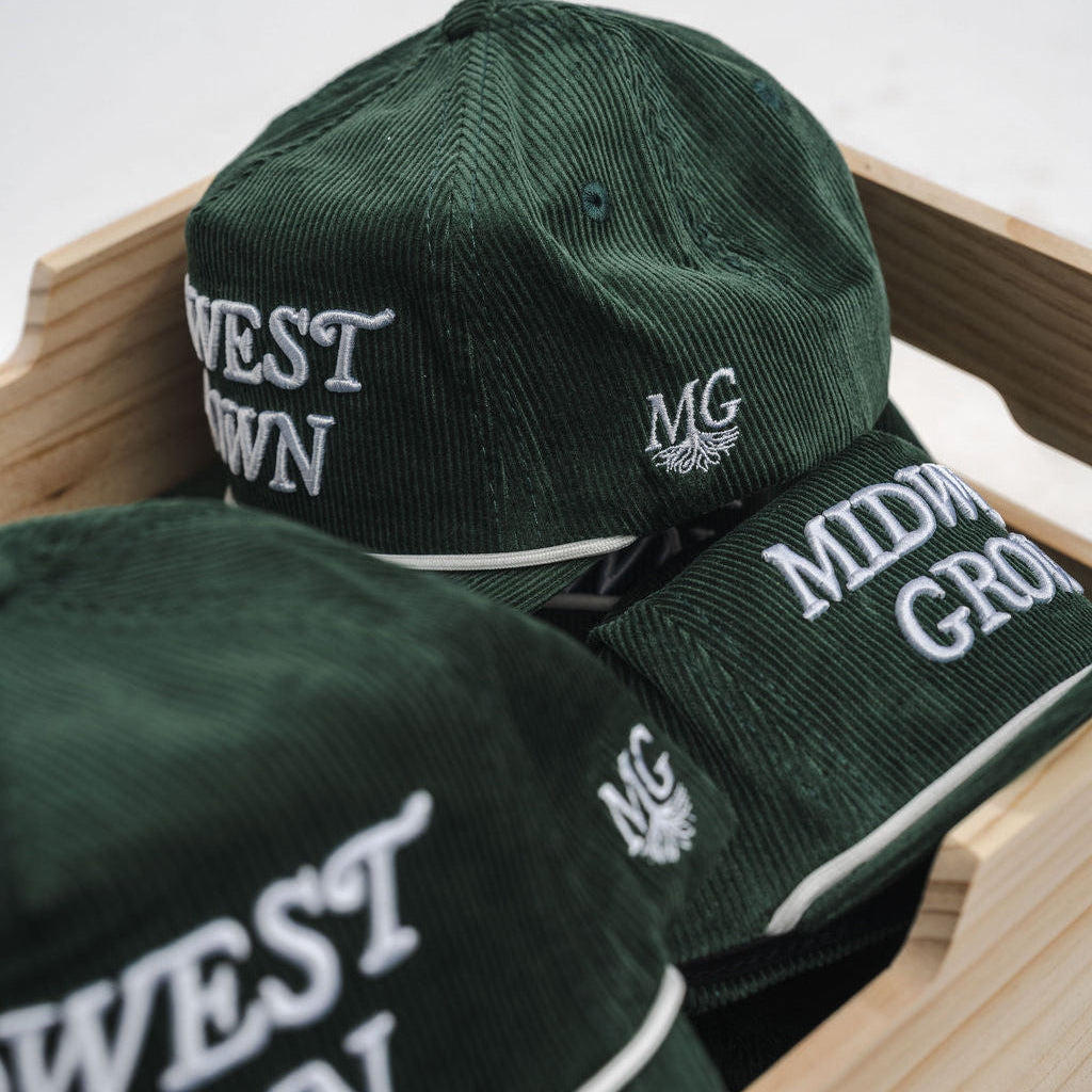 Green caps with 'West Grown' and 'Midwest Grown' text on a wooden surface.