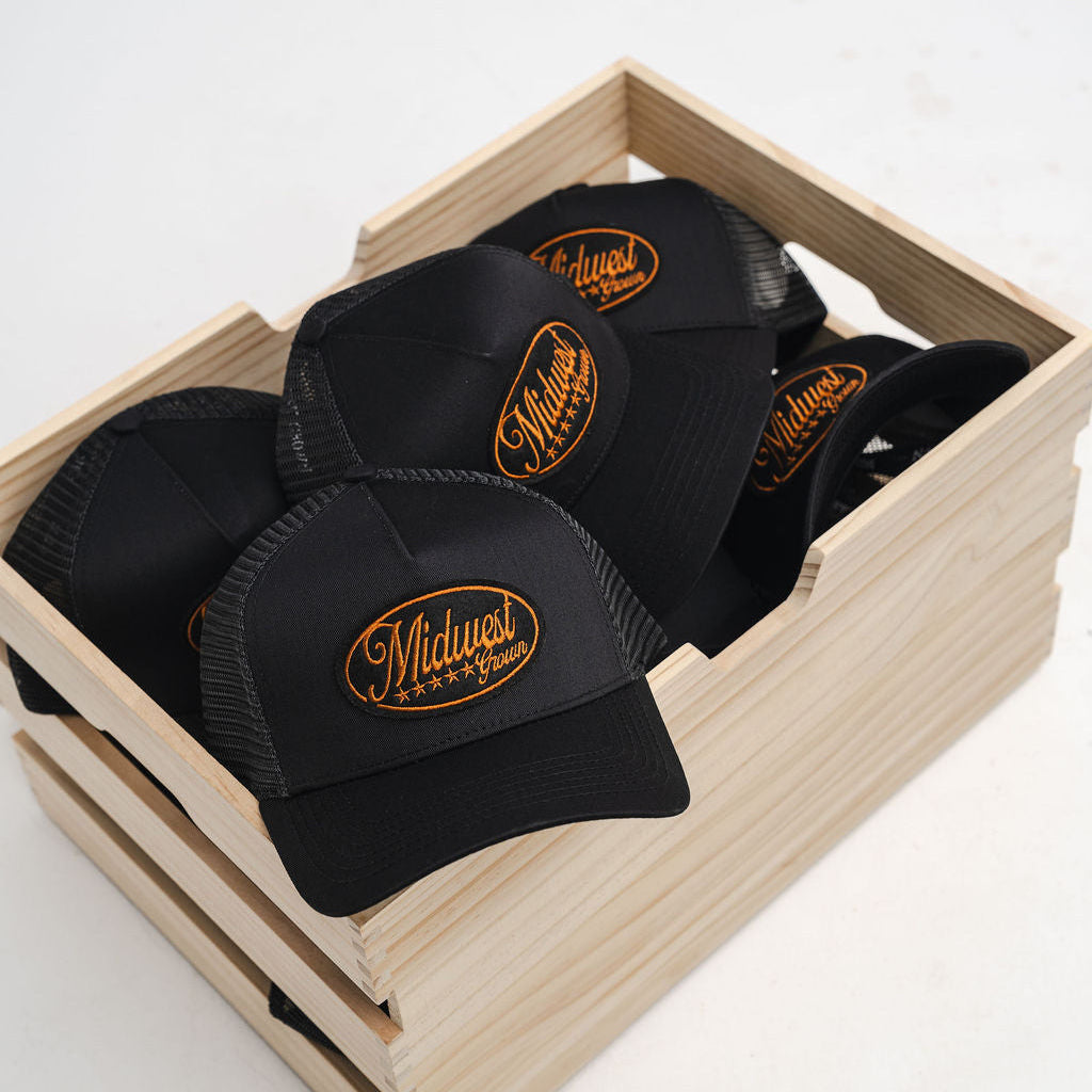Black Midwest Grown caps with a logo in a wooden crate on a white background
