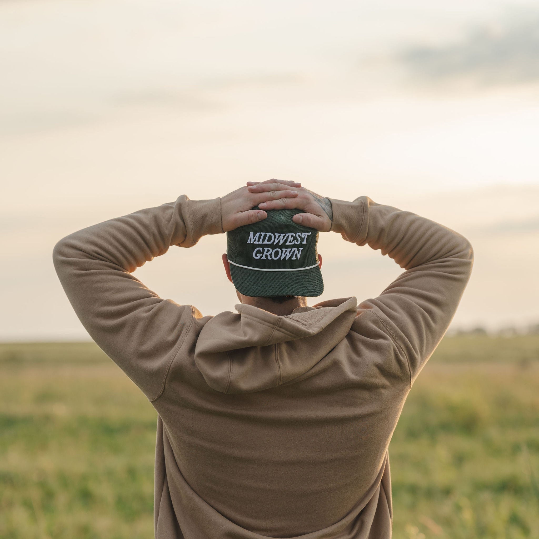 Person holding a cap with 'Midwest Crown' text in a field