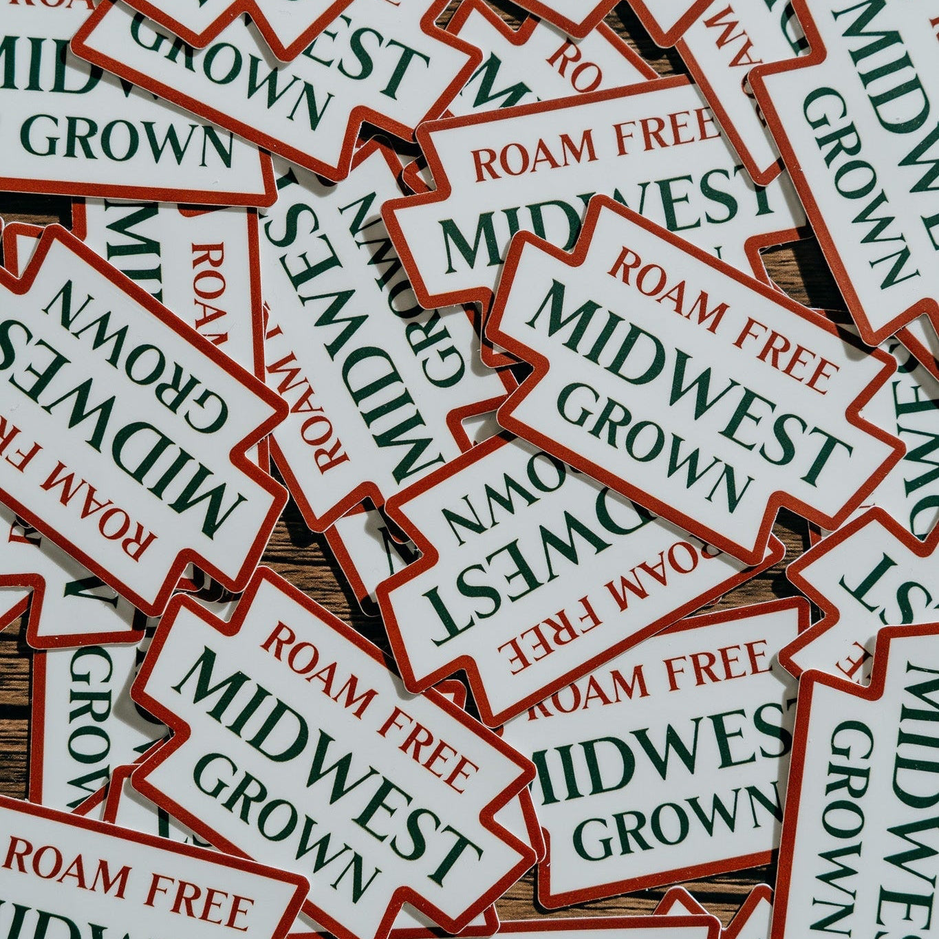 Stack of 'Midwest Grown' and 'Roam Free' stickers on a wooden surface.