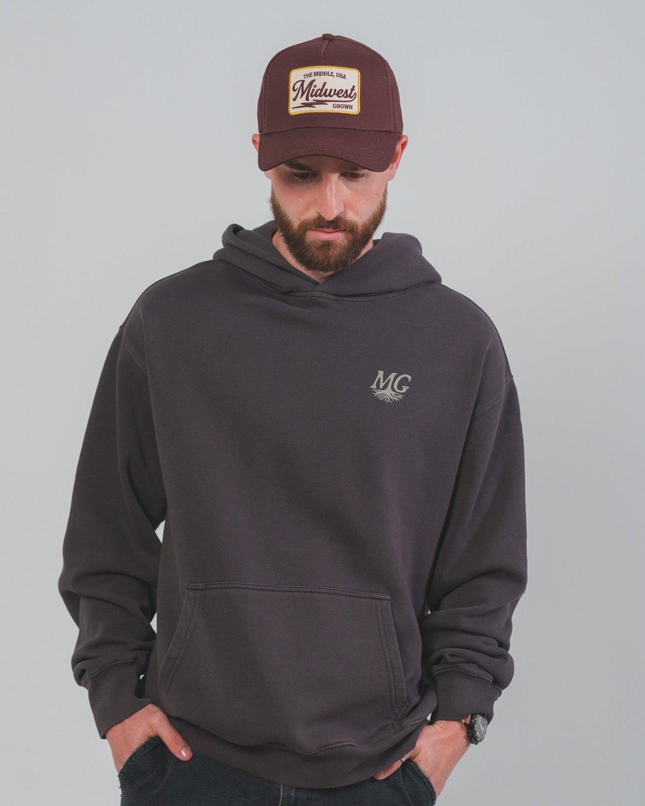 Man wearing a dark gray hoodie and maroon Midwest Grown cap with logo on a gray background