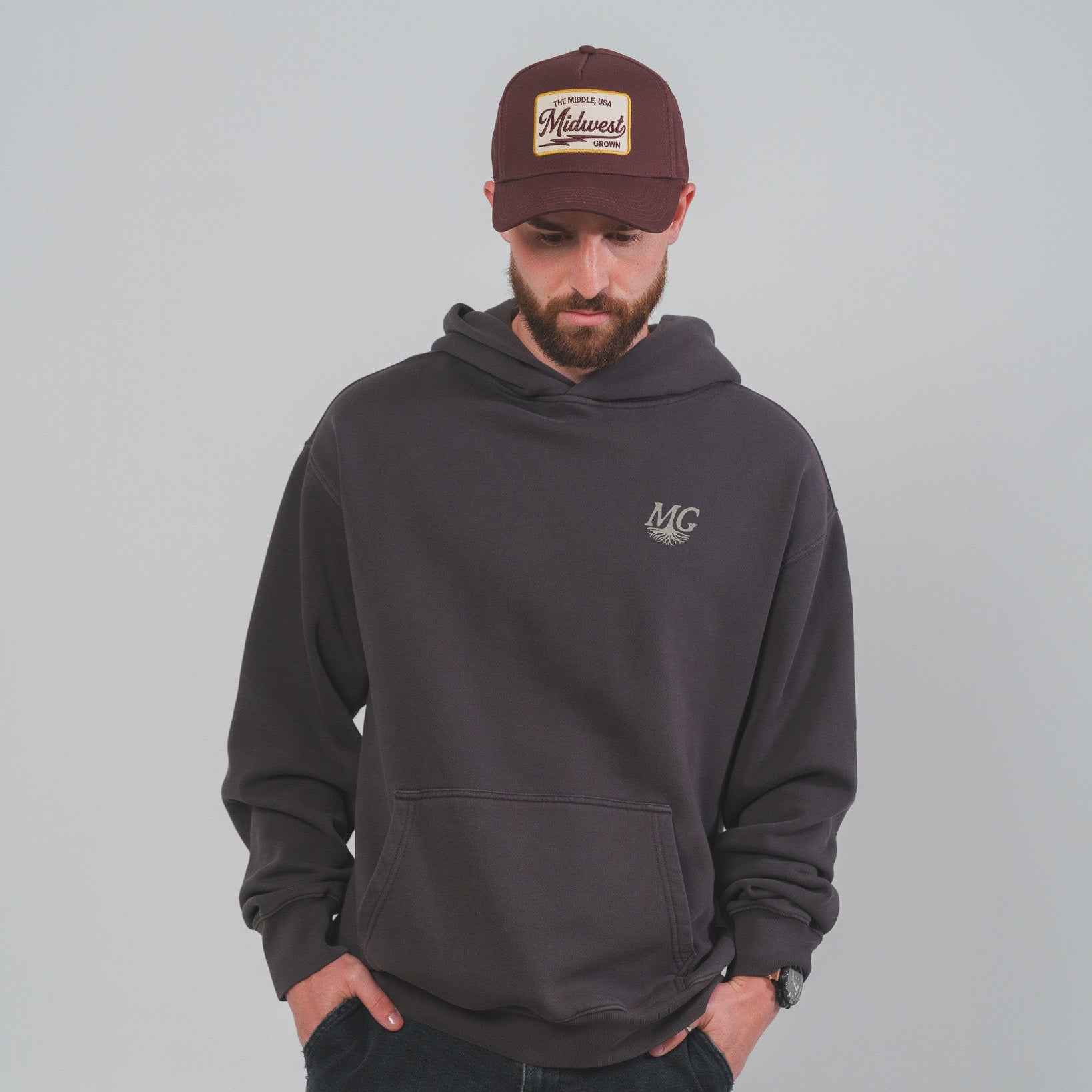 Man wearing a dark gray hoodie and maroon Midwest Grown cap with logo on a gray background