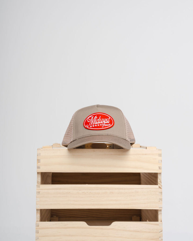Beige Midwest Grown cap with red logo on a wooden crate against a light gray background