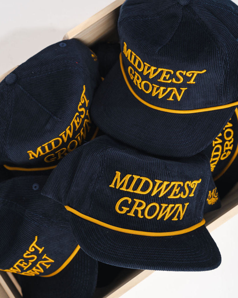 Box containing navy blue caps with 'Midwest Grown' text on a white background