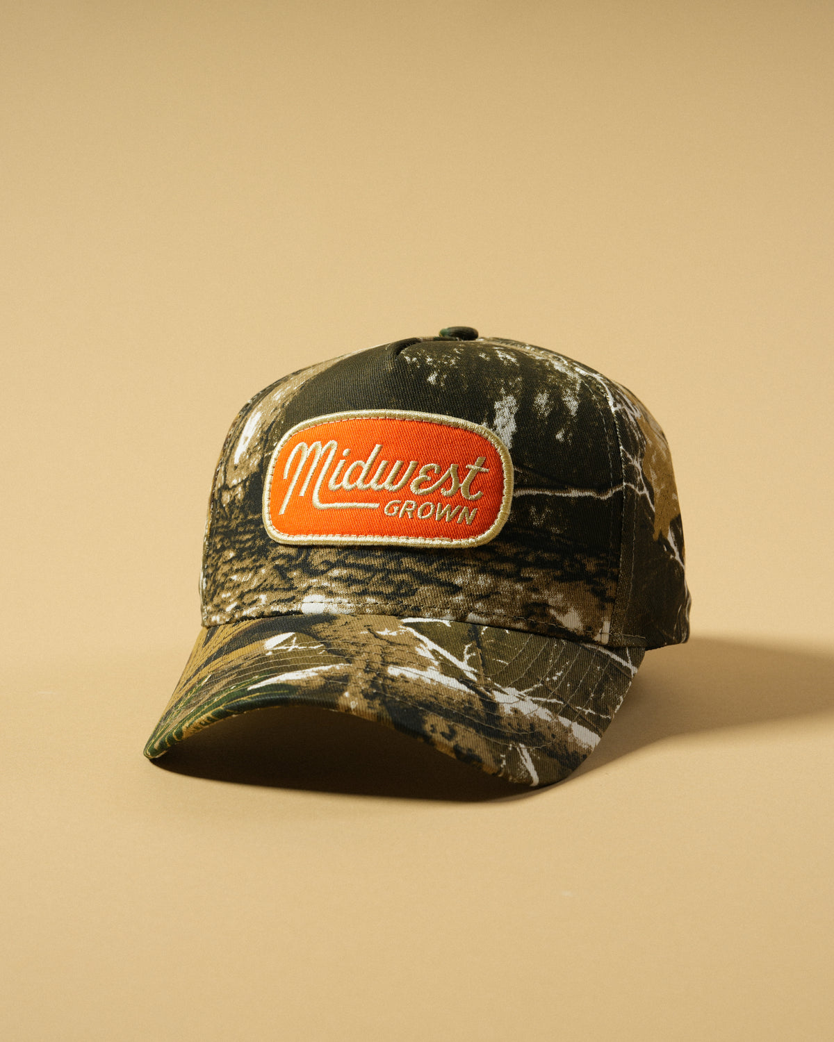 Front view of the Back Forty Camo Hat with an orange Midwest Grown patch and curved brim.
