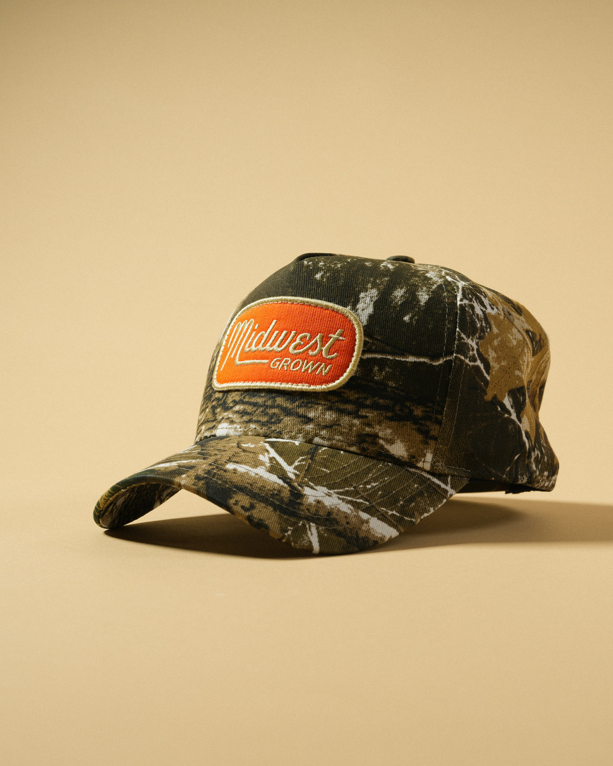 Side angle of the Back Forty Camo Hat showing the orange embroidered patch, camo crown, and curved brim.