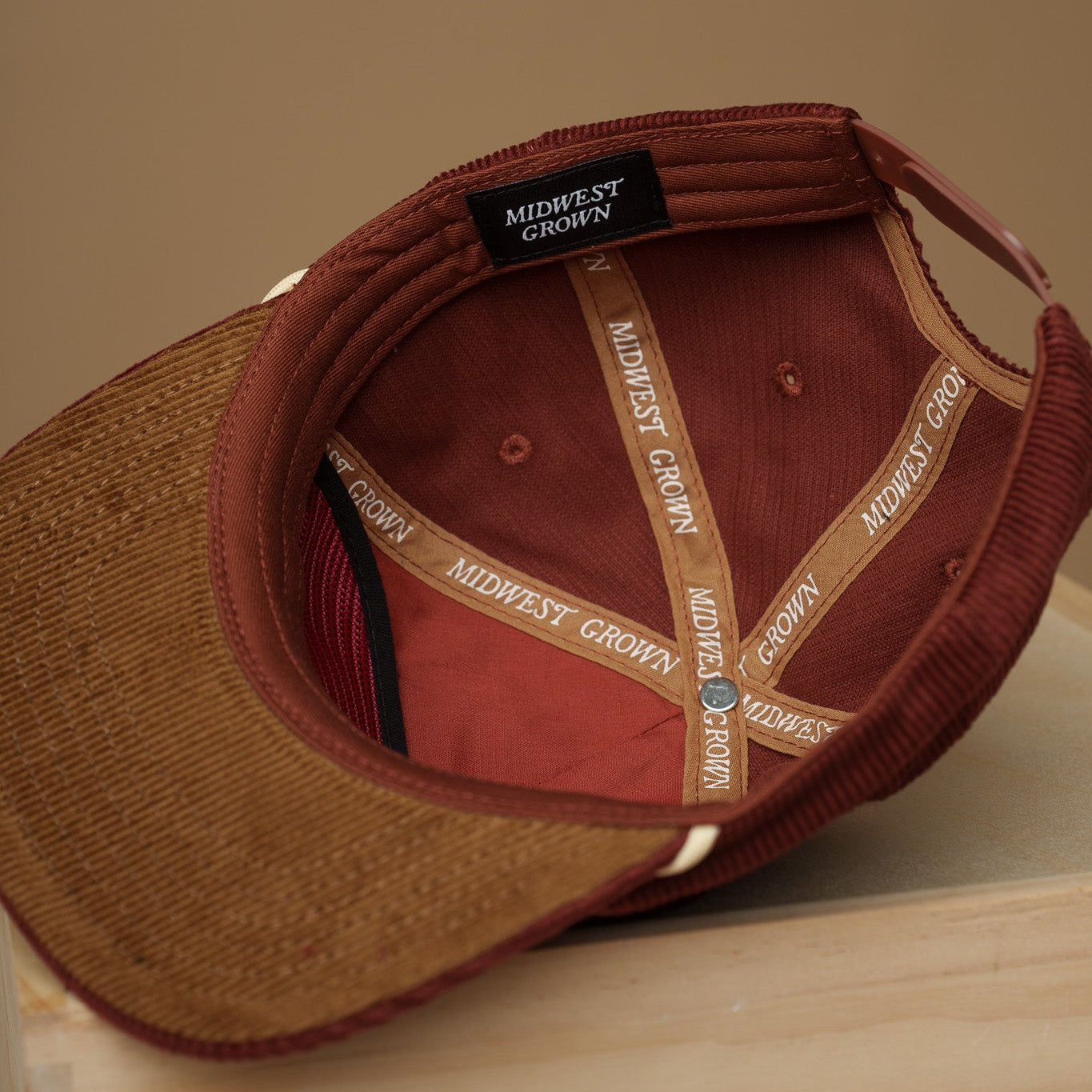 Maroon Midwest Grown baseball cap with visible branding on a wooden surface and beige background