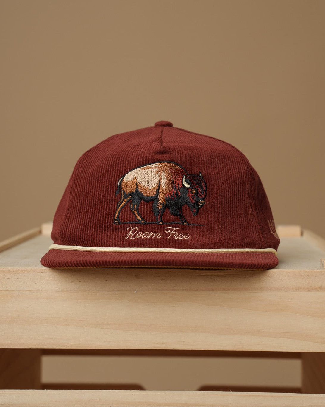 Maroon Midwest Grown cap with a bison design on a wooden surface against a beige background