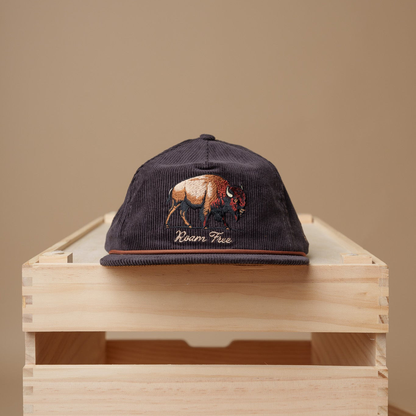 Midwest Grown Cap with a bison design on a wooden crate against a beige background