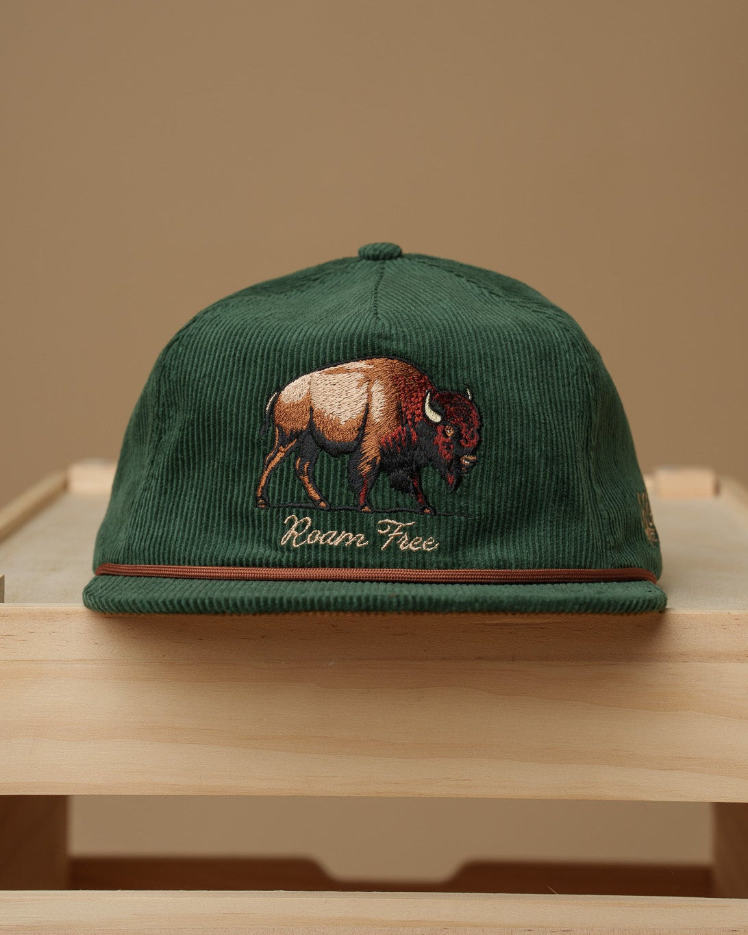 Midwest Grown Green cap with a bison design on a wooden crate against a beige background