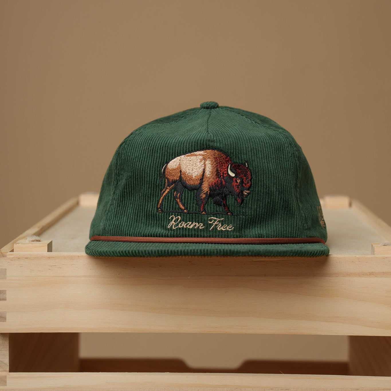 Midwest Grown Green cap with a bison design on a wooden crate against a beige background