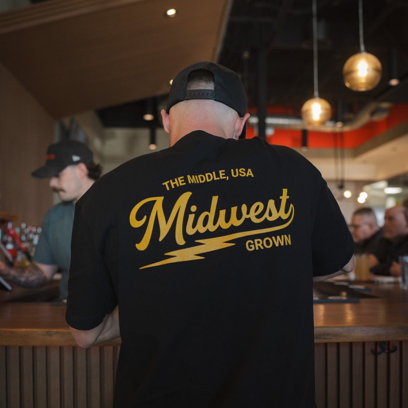 Person wearing a black t-shirt with 'Midwest Grown' text in a casual setting