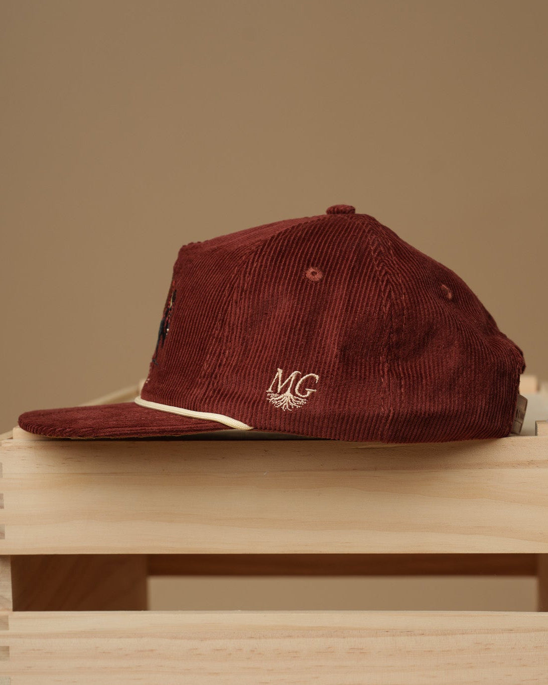 Maroon cap with a Midwest Grown logo on top of a wooden crate against a beige background