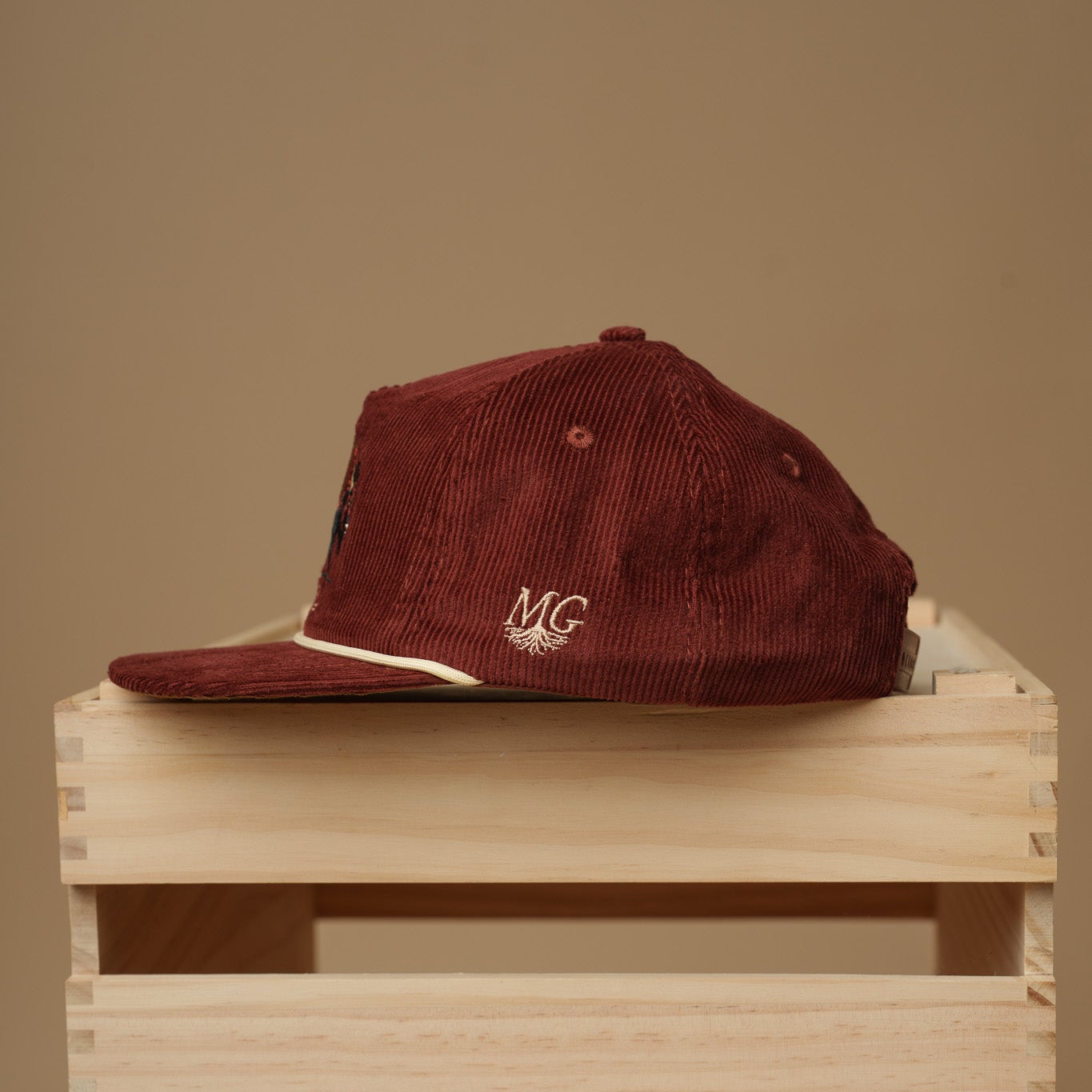 Maroon cap with a Midwest Grown logo on top of a wooden crate against a beige background