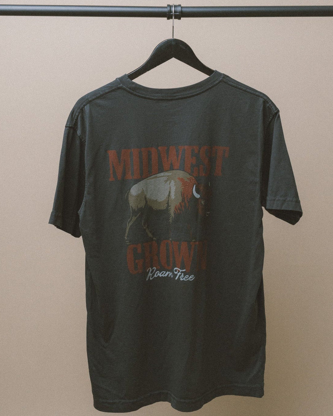 Black Midwest Grown t-shirt with Bison graphic design and text on a hanger against a beige wall