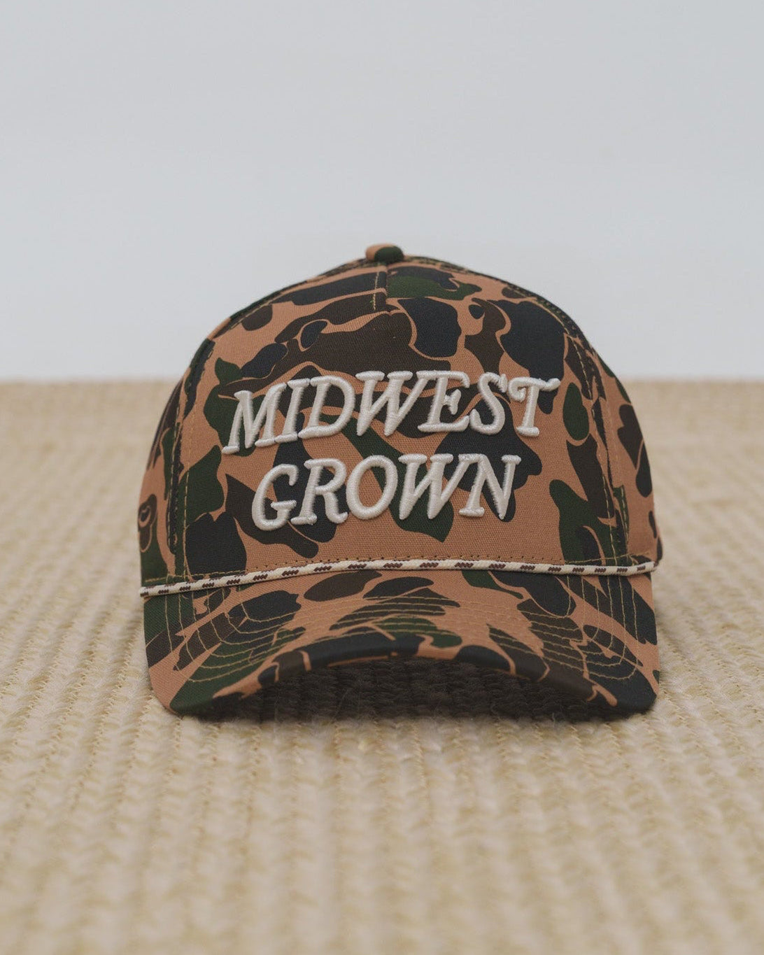 Duck Camouflage-patterned cap with 'Midwest Grown' text on a textured surface.