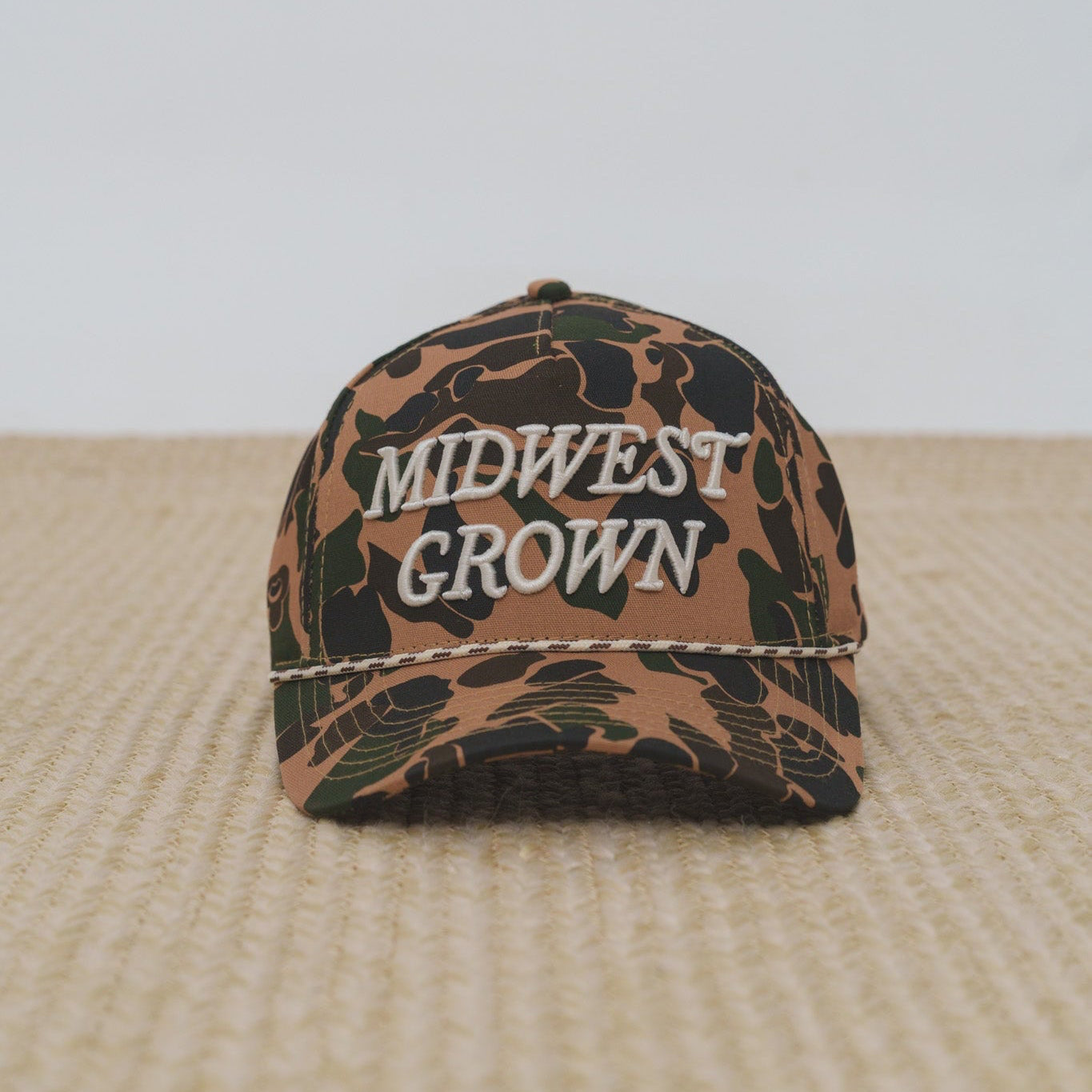 Duck Camouflage-patterned cap with 'Midwest Grown' text on a textured surface.